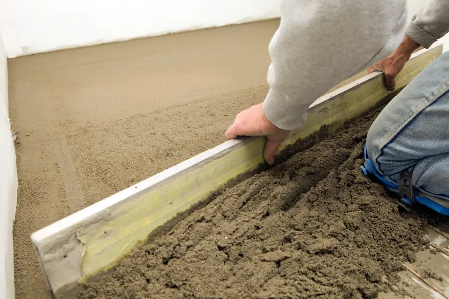 Handwerker zieht frisch eingebrachten Estrich mit einer Abziehlatte glatt
