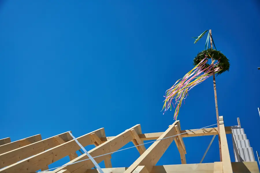 Richtkranz mit bunten Bändern auf einem neuen Holzdachstuhl vor blauem Himmel