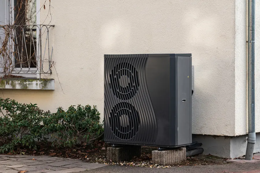 Außeneinheit einer Luft-Wasser-Wärmepumpe auf Sockelsteinen vor der verputzten Wand eines Altbaus