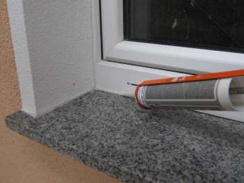 Silikon wird mit der Kartuschenpistole zwischen Granit-Fensterbank und Fensterrahmen gespritzt