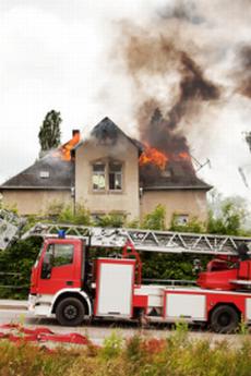 Brennendes Wohnhaus, davor ein Feuerwehrfahrzeug mit Drehleiter