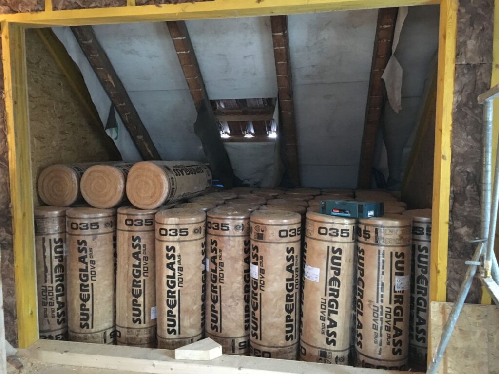 Gestapelte Rollen Glaswolle der Wärmeleitgruppe 035 auf einem Dachboden, bereit für die Dämmung