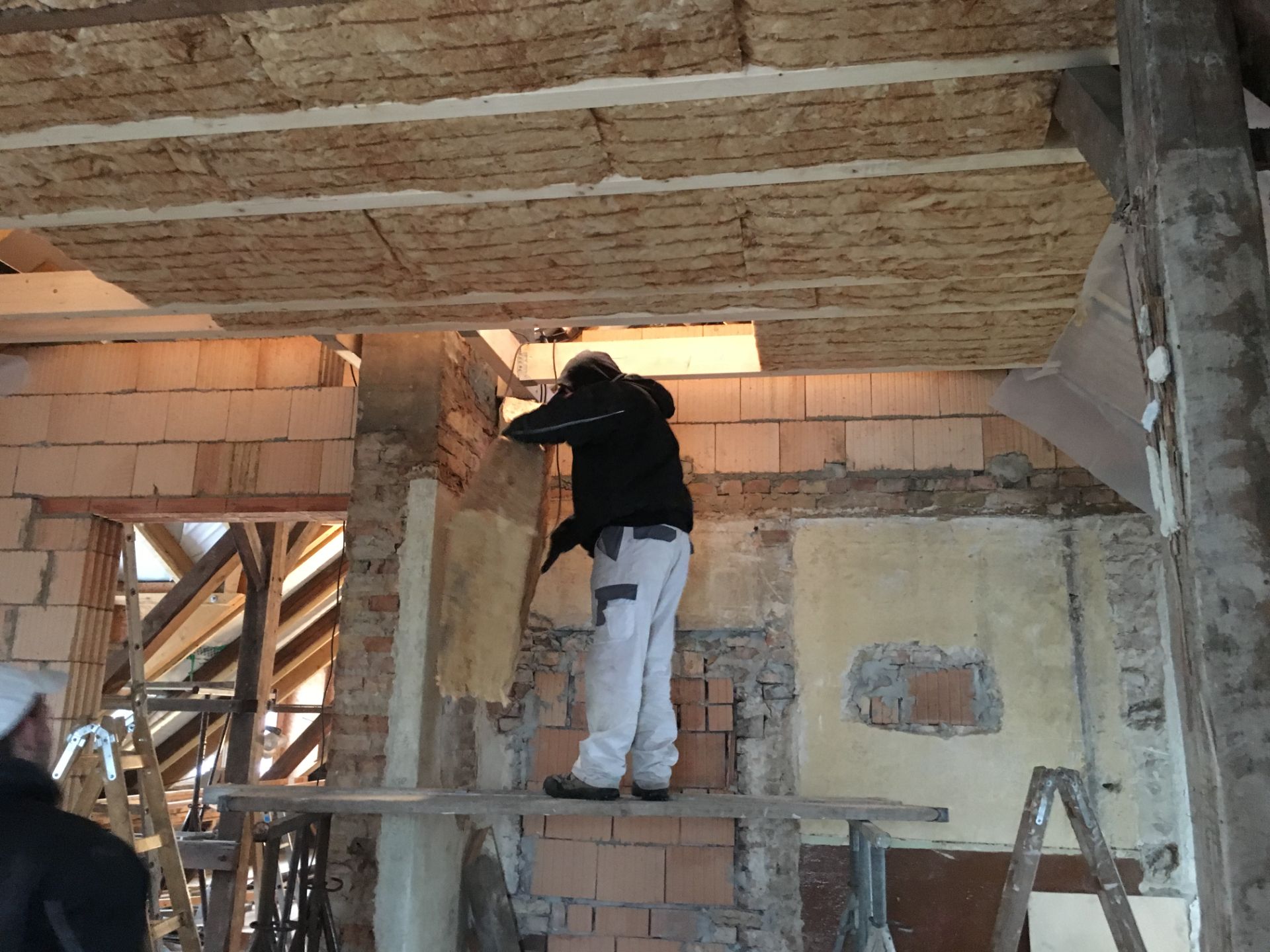 Handwerker dämmt eine Holzbalkendecke im Altbau von unten mit Mineralwolle zwischen den Balken